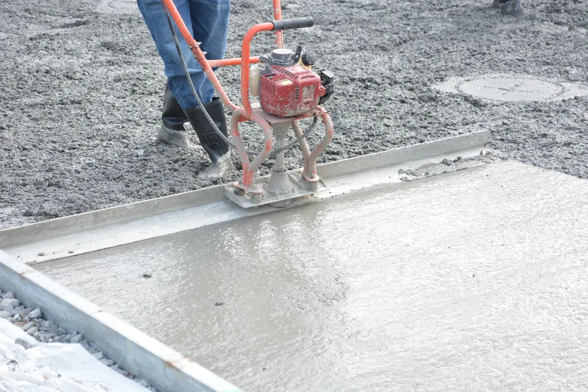Worker running a vibrating power screed across a freshly poured concrete slab